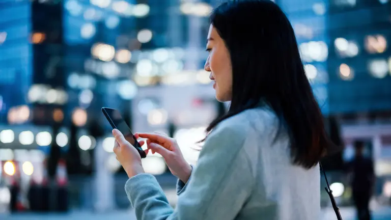 A woman with a cell phone in her hand, standing on a busy square in the city